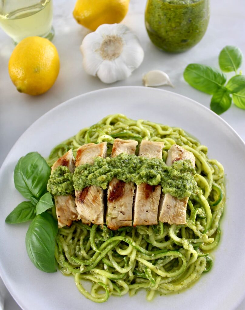 overhead view of Grilled Lemon Chicken Pesto Zoodles on white plate with fresh basil garnish