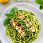 Grilled Lemon Chicken Pesto Zucchini Noodles on white plate with chicken on top and basil leaf on side