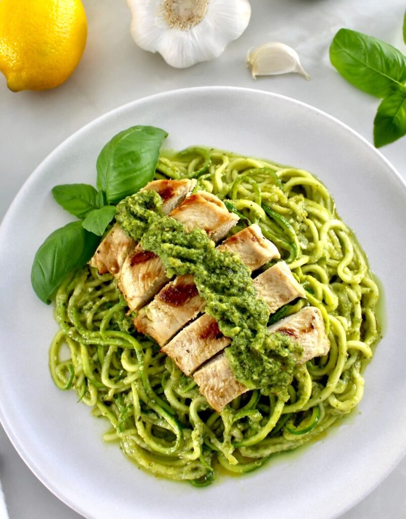Grilled Lemon Chicken Pesto Zucchini Noodles on white plate with chicken on top and basil leaf on side