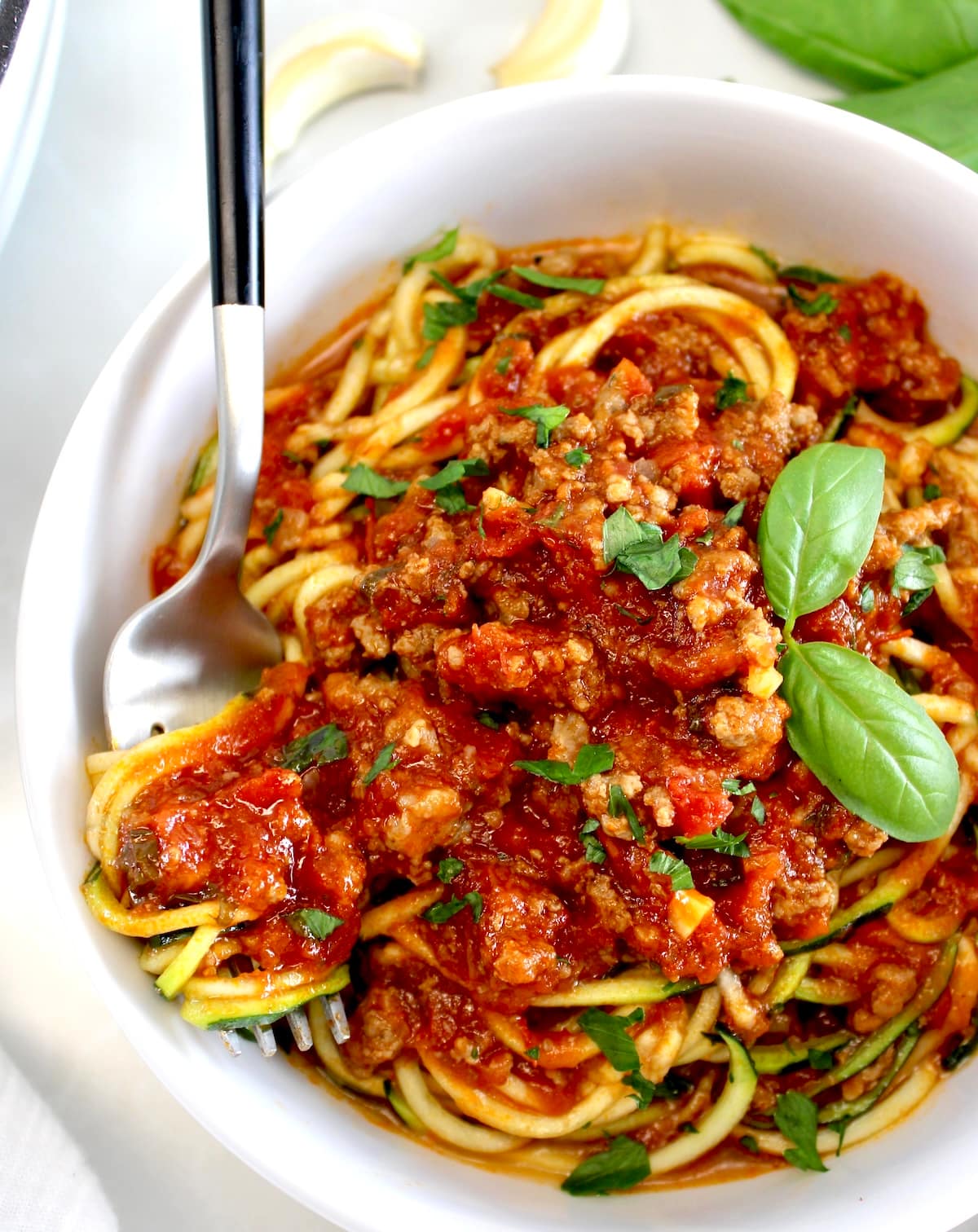 Italian Meat Sauce over zucchini noodles in white bowl with forkful on side