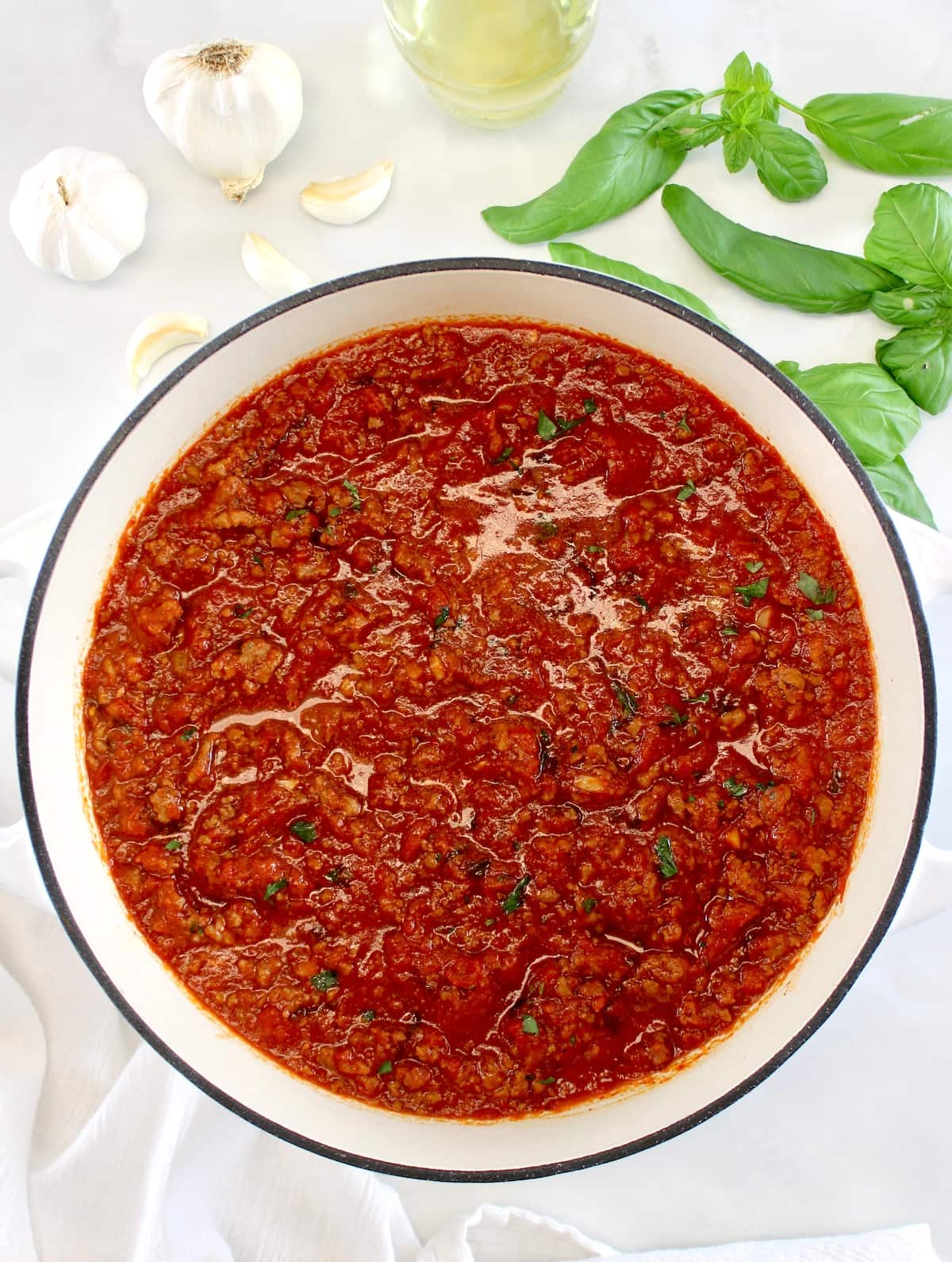 overhead view of Italian Meat Sauce in white pot with basil and garlic in back