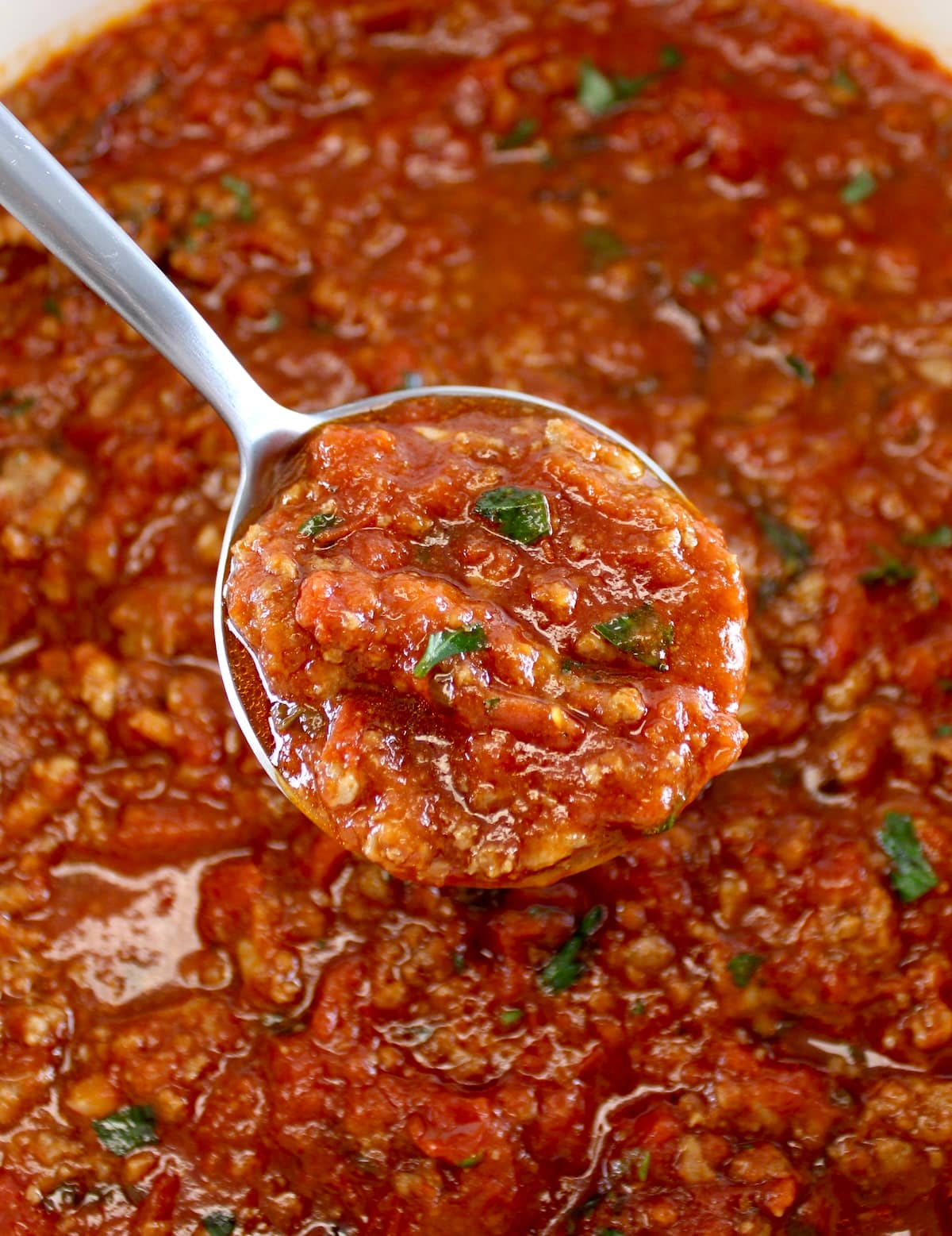 holding up spoonful of Italian Meat Sauce over pot