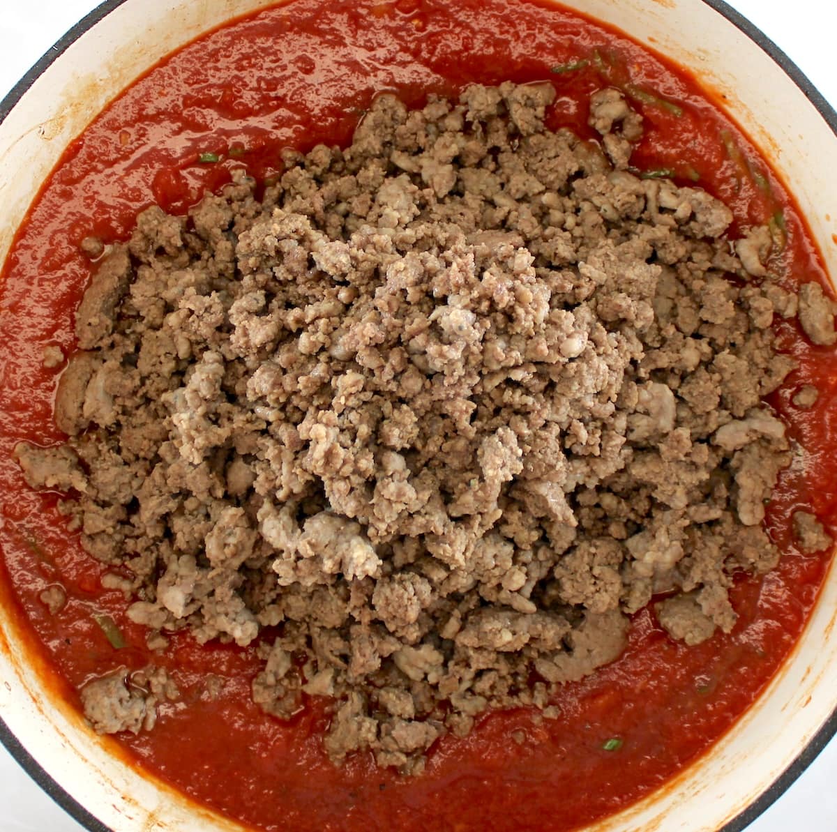 browned ground beef and sausage on top of tomato sauce in pot