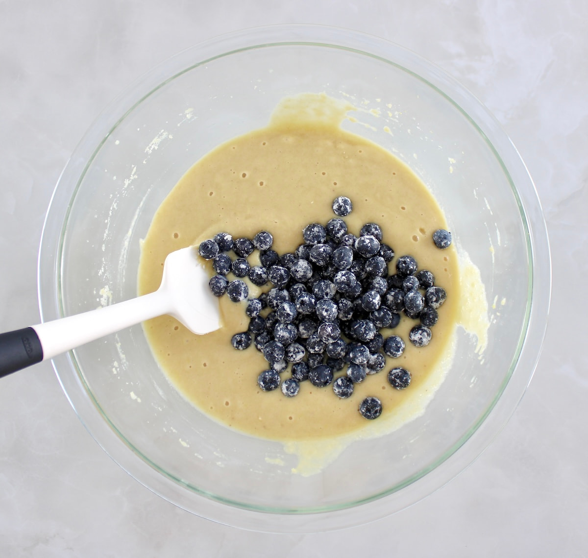 Keto Blueberry Crumb Loaf batter in glass bowl with blueberries on top and white spatula on side
