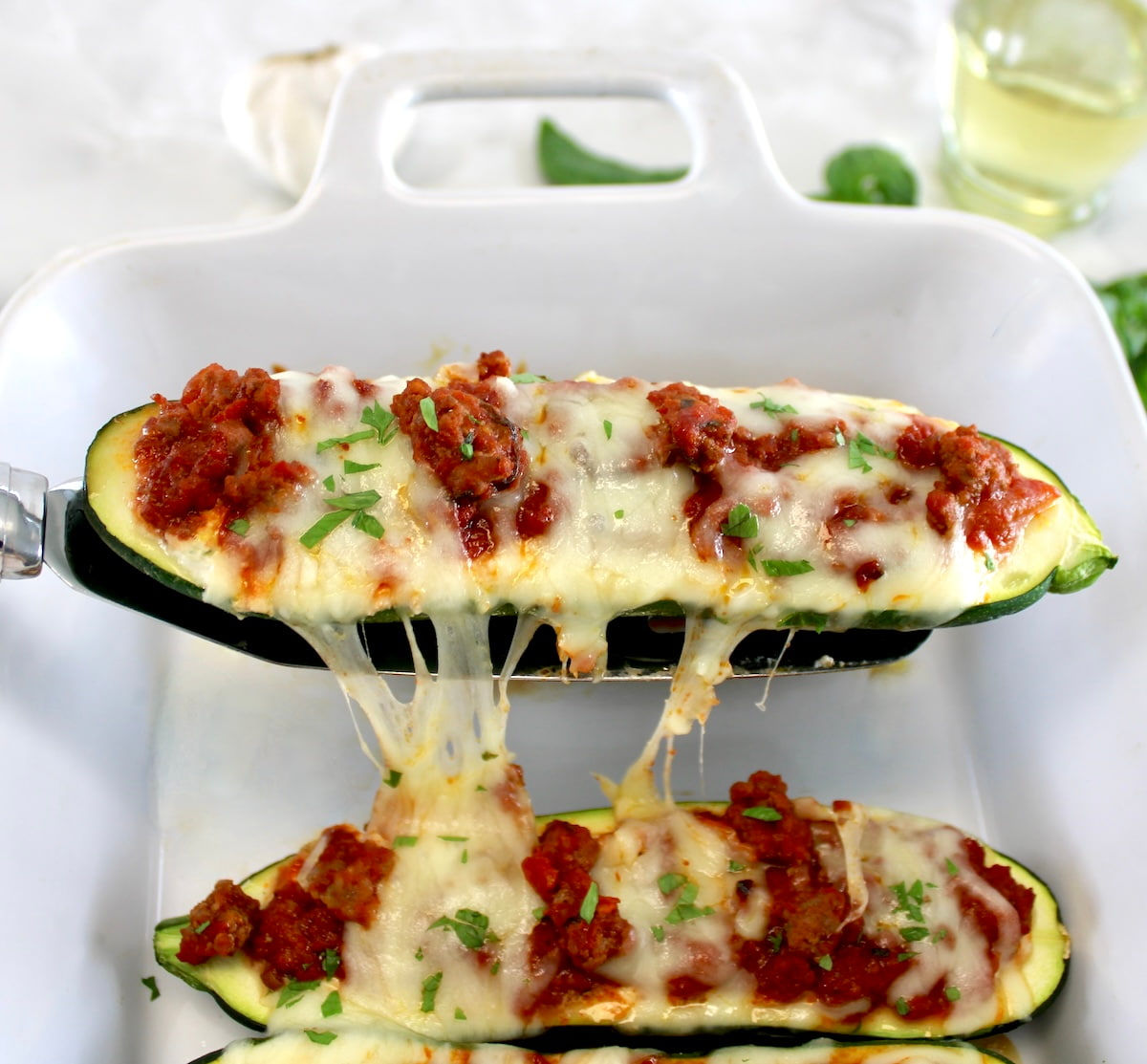 spatula lifting Lasagna Stuffed Zucchini Boat out of white casserole with cheese pull