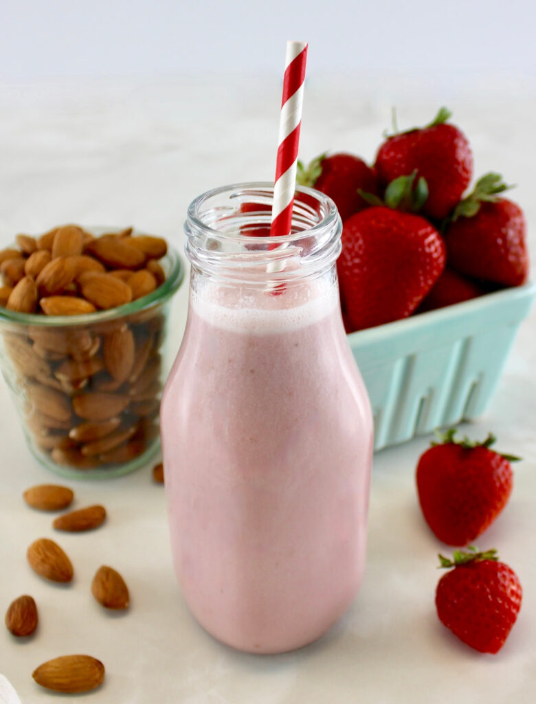 Strawberry Almond Milk in glass bottle with red and white straw, strawberries and almonds in back