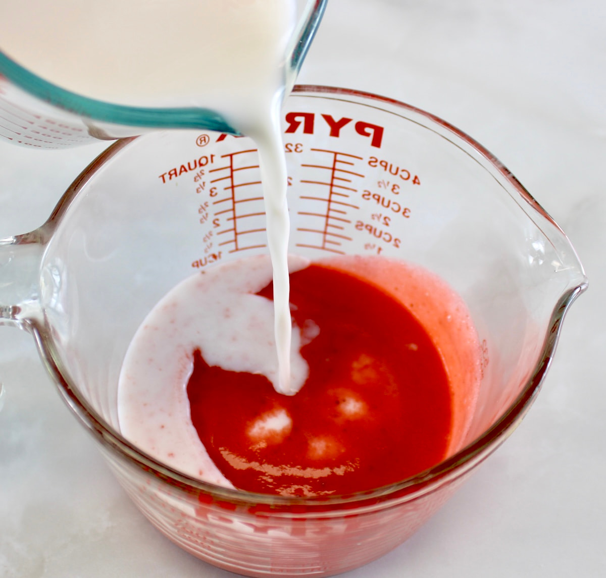 almond milk being poured into glass measuring bowl with strawberry puree