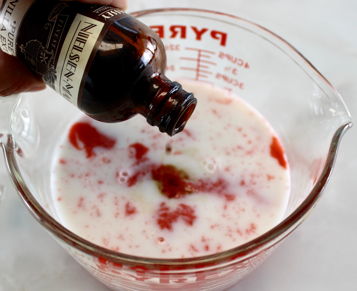 vanilla extract being poured into measuring bowl with strawberry almond milk