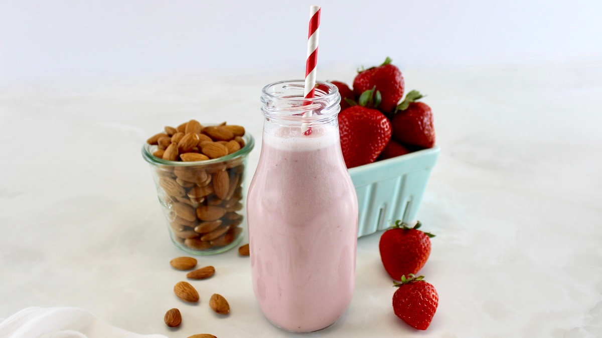 side view of Strawberry Almond Milk in glass bottle with red and white straw