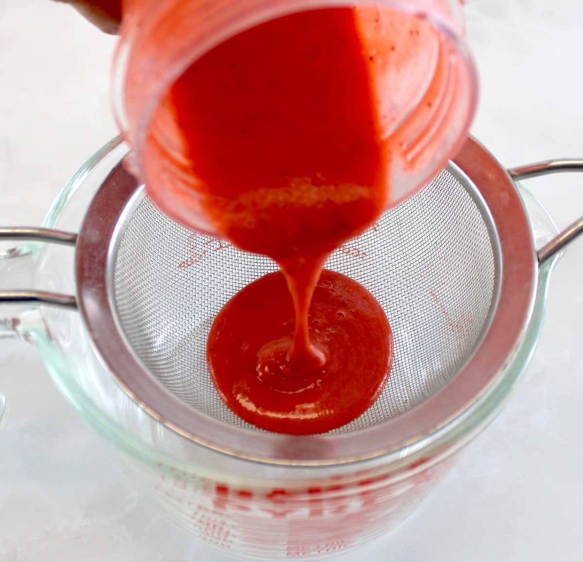strawberry puree being poured through sieve