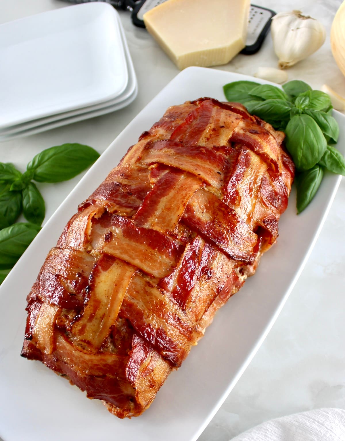 overhead view of Bacon Wrapped Cheese Stuffed Italian Meatloaf on white plate with fresh basil on top