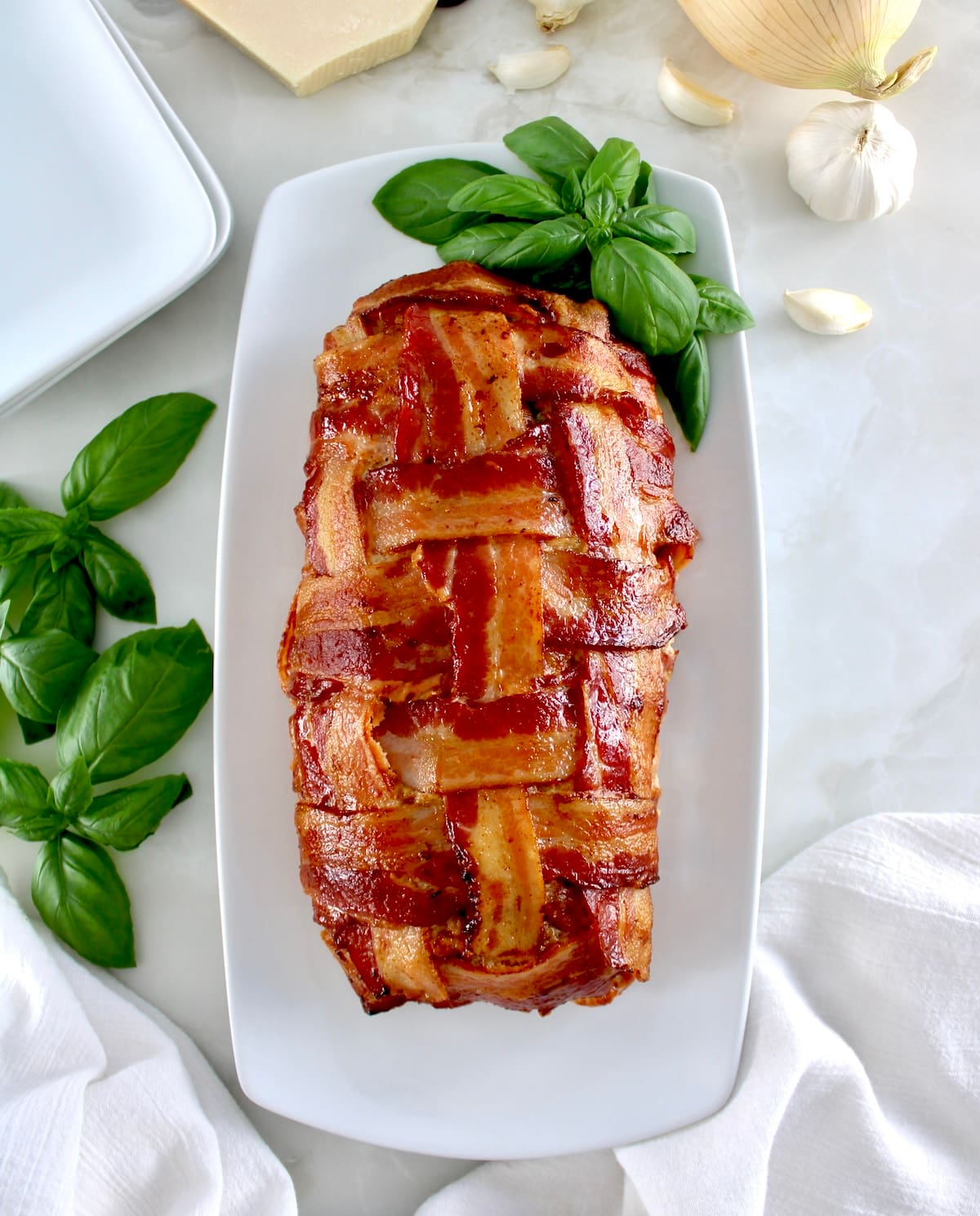 overhead view of Bacon Wrapped Cheese Stuffed Italian Meatloaf on white plate with fresh basil leaves