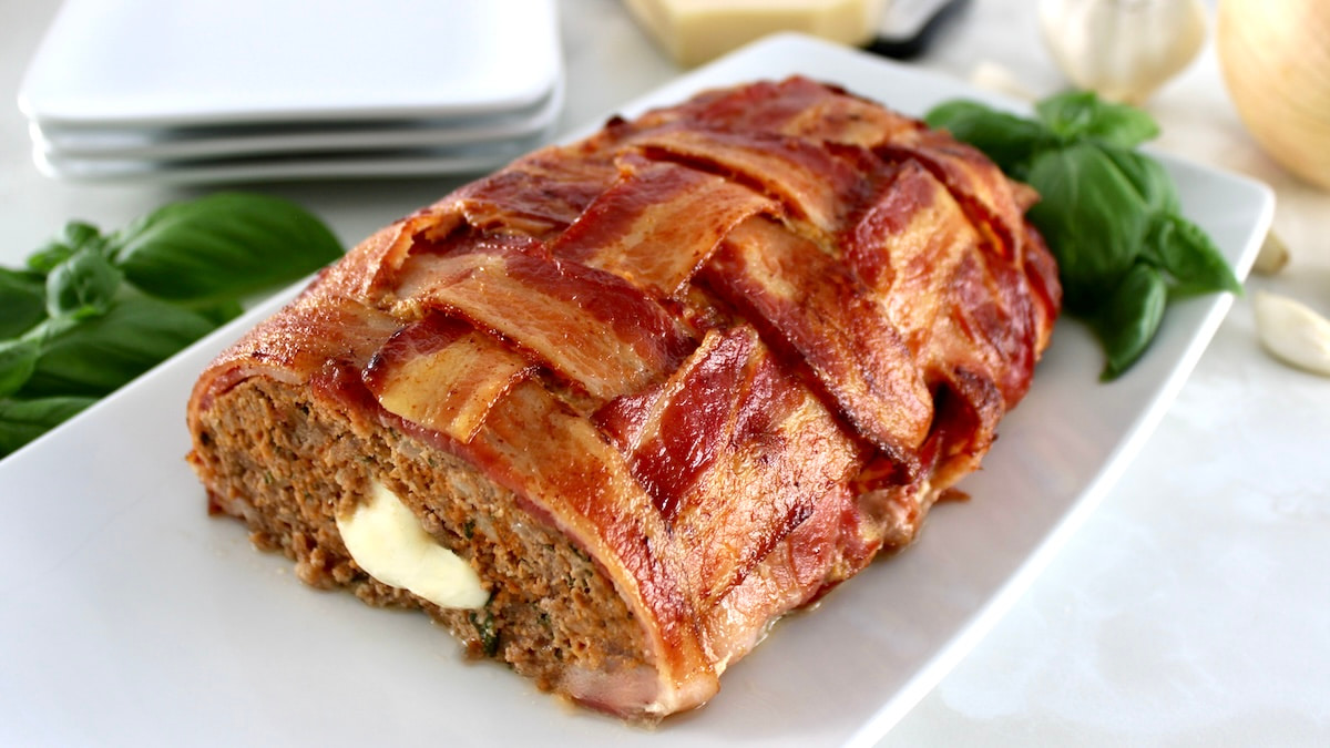 Bacon Wrapped Cheese Stuffed Italian Meatloaf with end cut off and cheese oozing out the middle on white plate