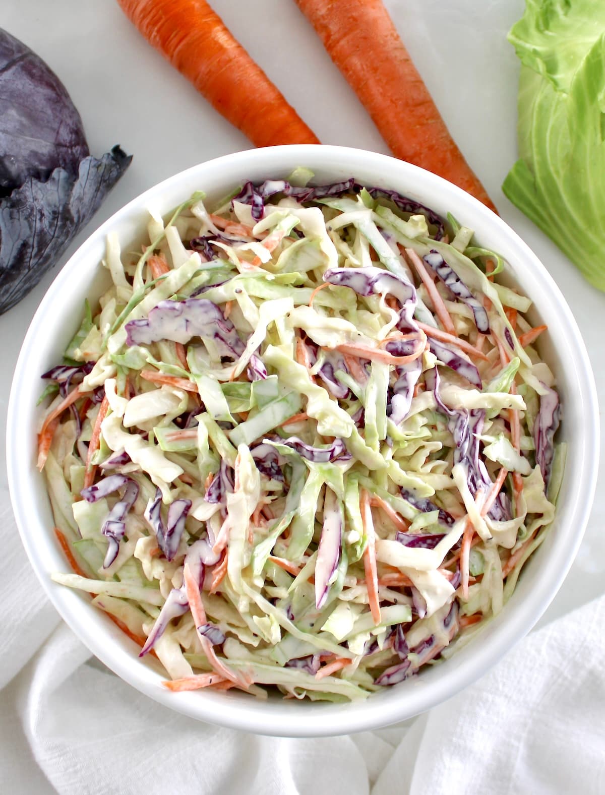 overhead view of Easy Keto Coleslaw in white bowl with carrots and cabbage in back