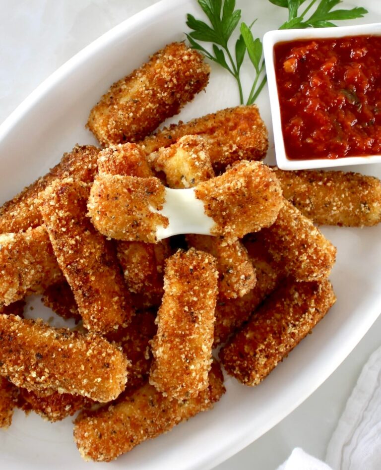 keto mozzarella cheese sticks on white platter with marinara on side and one cheese stick pulled apart