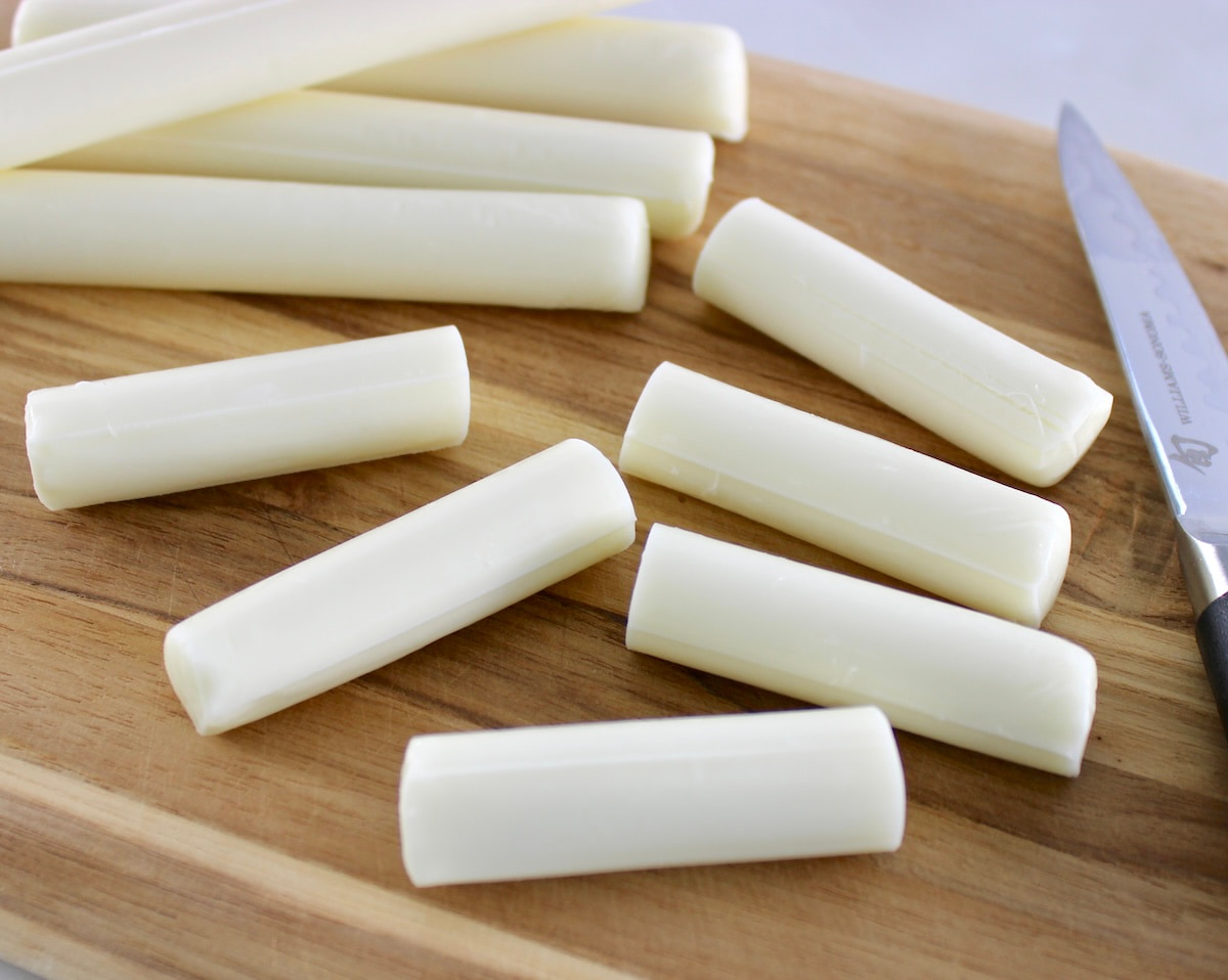 cut up mozzarella sticks on cutting board with knife