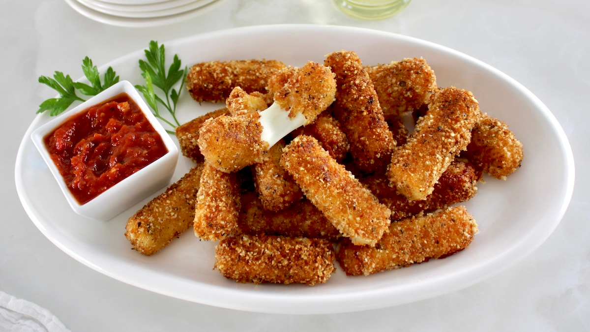 Keto Mozzarella Sticks on platter with one pulled apart and marinara on side