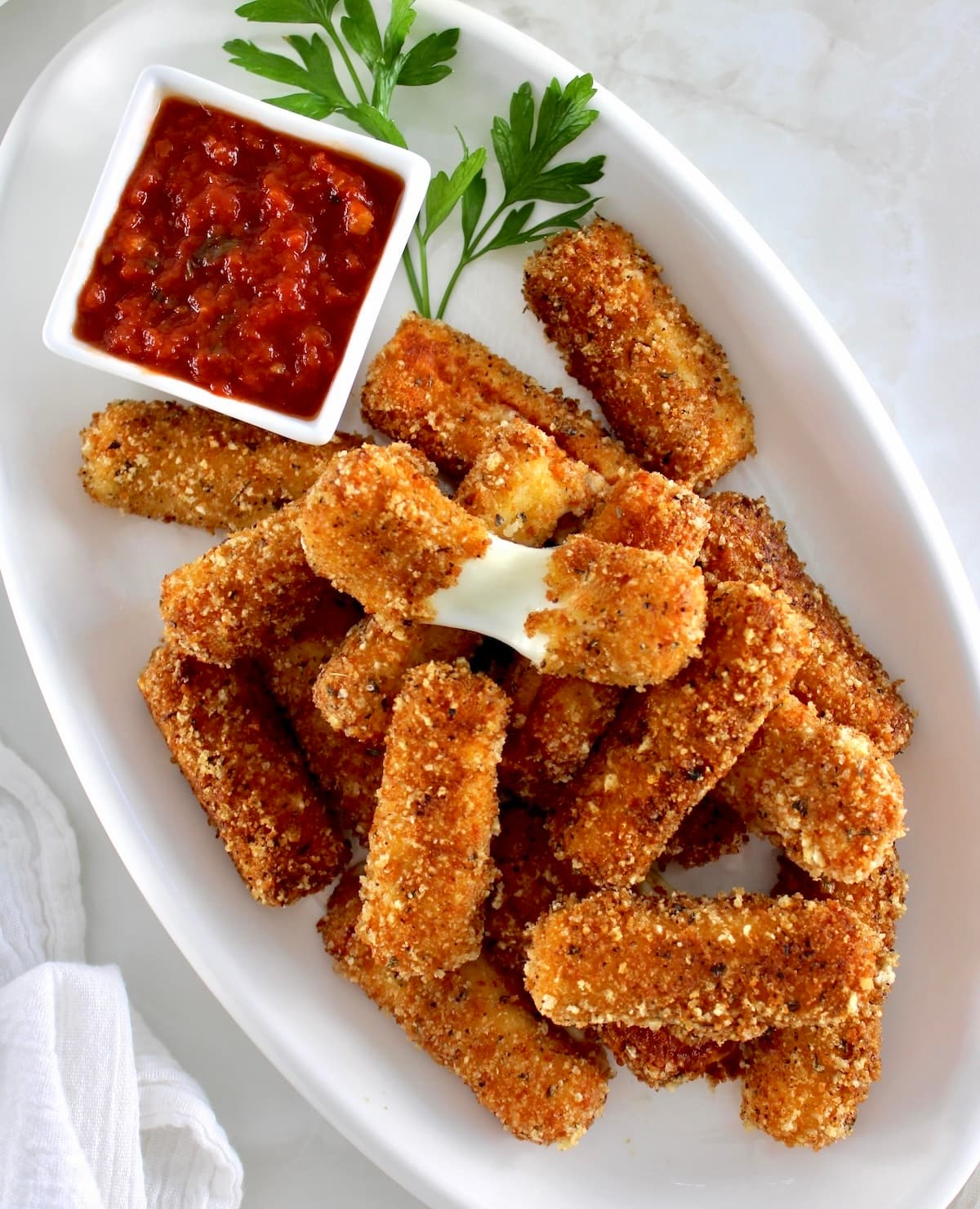 overhead view of Keto Mozzarella Sticks on white platter with marinara sauce