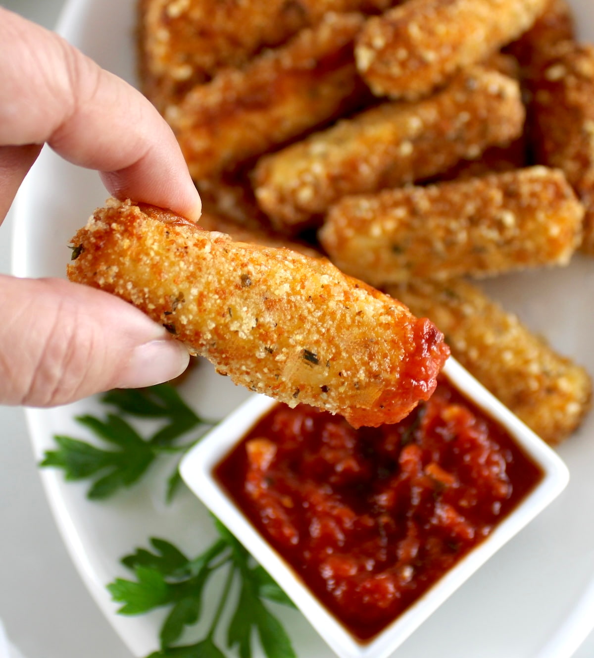 holding up Keto Mozzarella Stick dipping in marinara