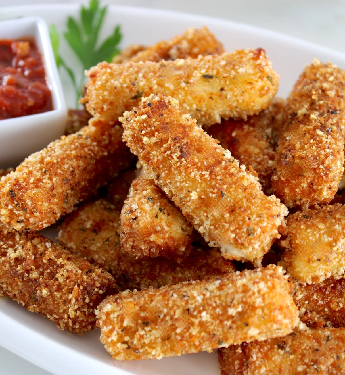 Keto Mozzarella Sticks stacked up on white platter with marinara sauce on side