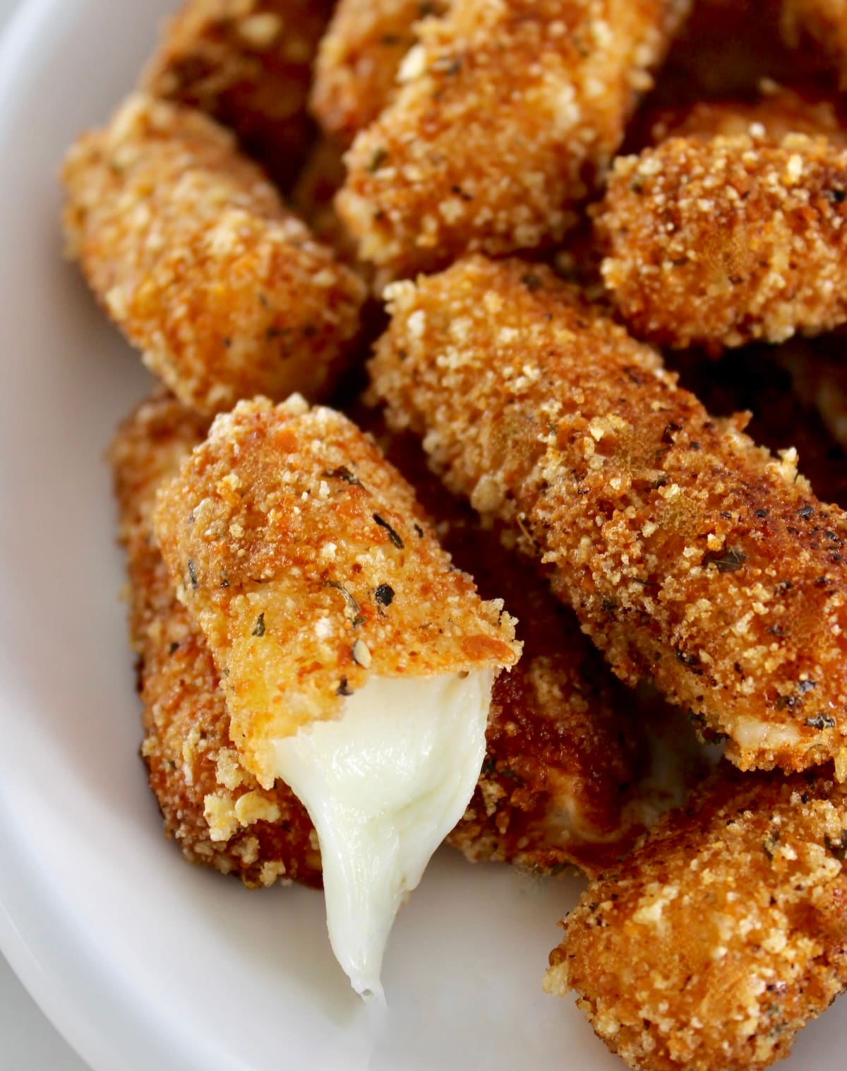 closeup of Keto Mozzarella Sticks on white plate with one cut open and cheese oozing out