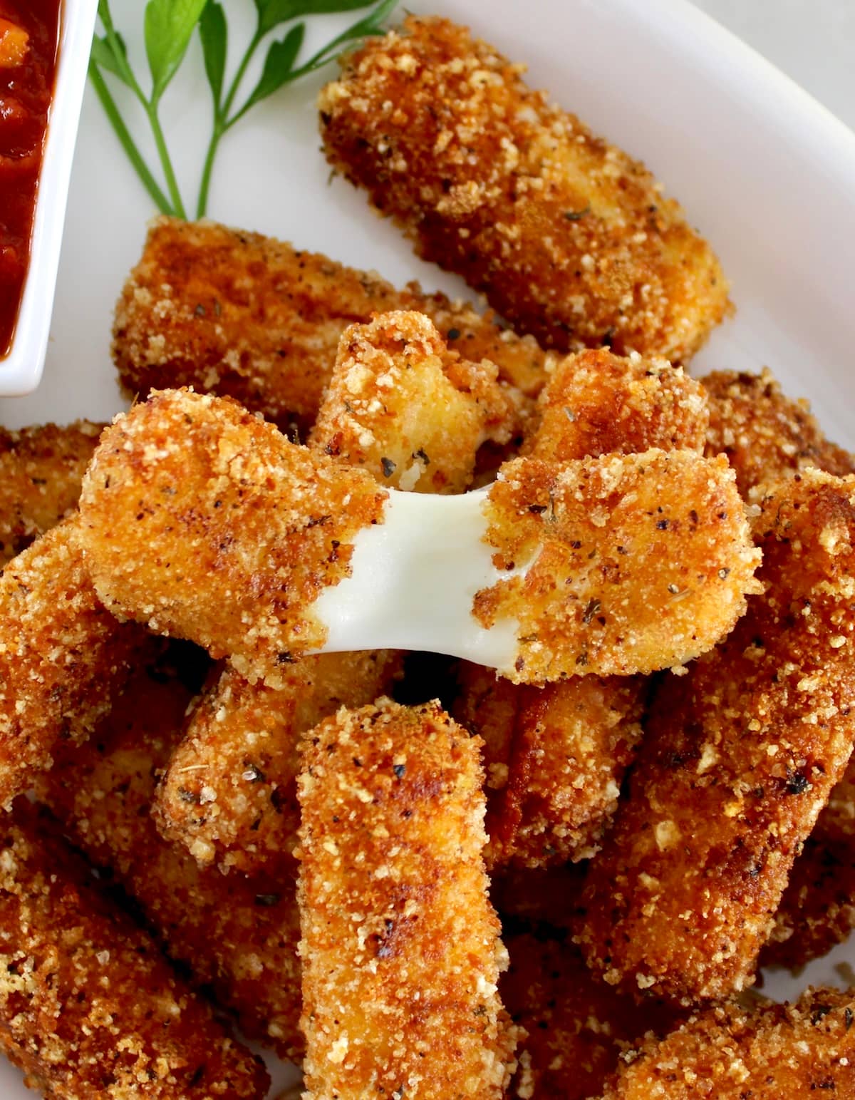closeup of Keto Mozzarella Sticks on white plate with one pulled apart