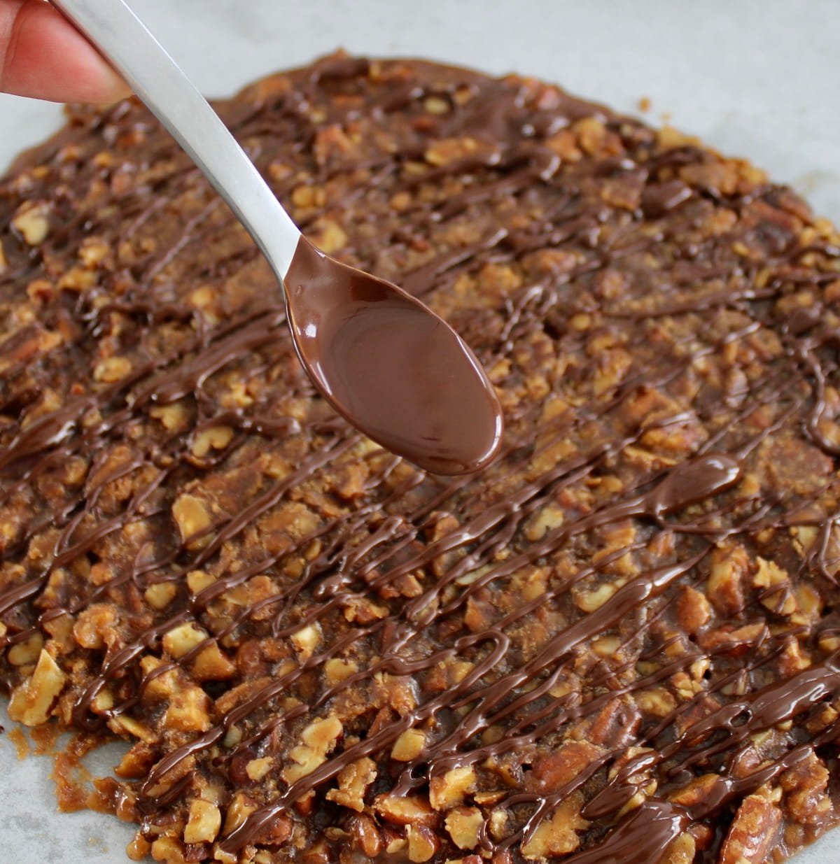 spoon holding melted chocolate with Keto Pecan Praline Bark in back