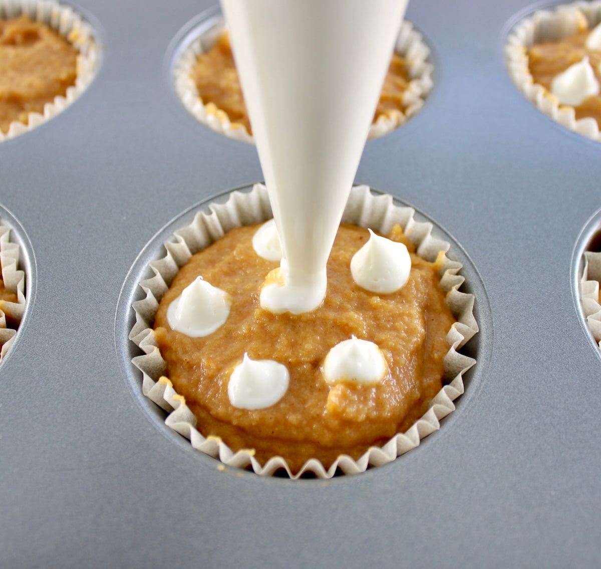 cream cheese filling being piped onto pumpkin muffins batter in muffin pan