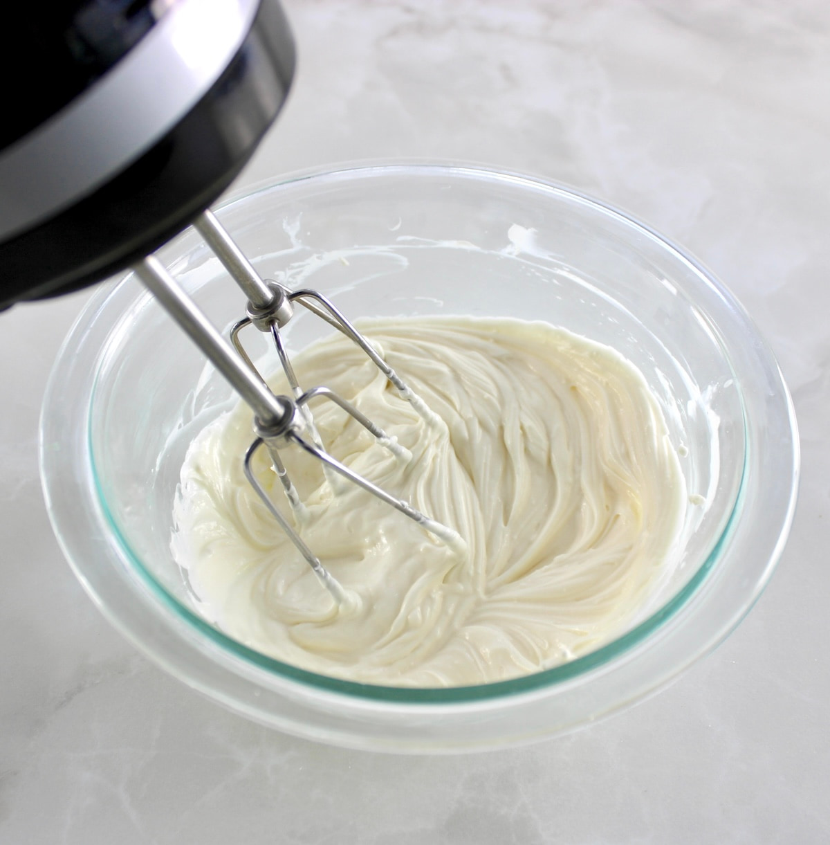 mixing cream cheese filling in glass bowl with hand mixer