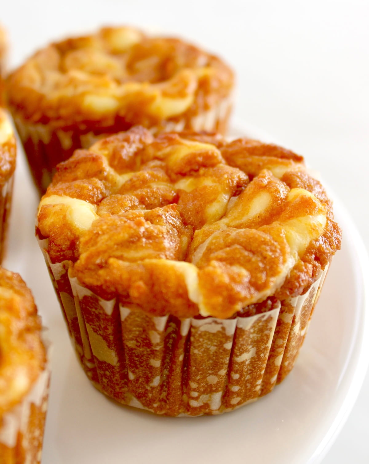 closeup of 2 Keto Pumpkin Cream Cheese Swirl Muffins on white plate