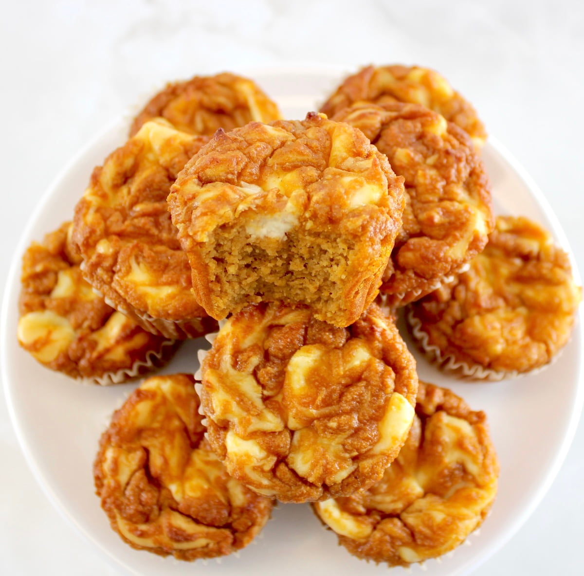 Keto Pumpkin Cream Cheese Swirl Muffins stacked up with bite missing from center muffin