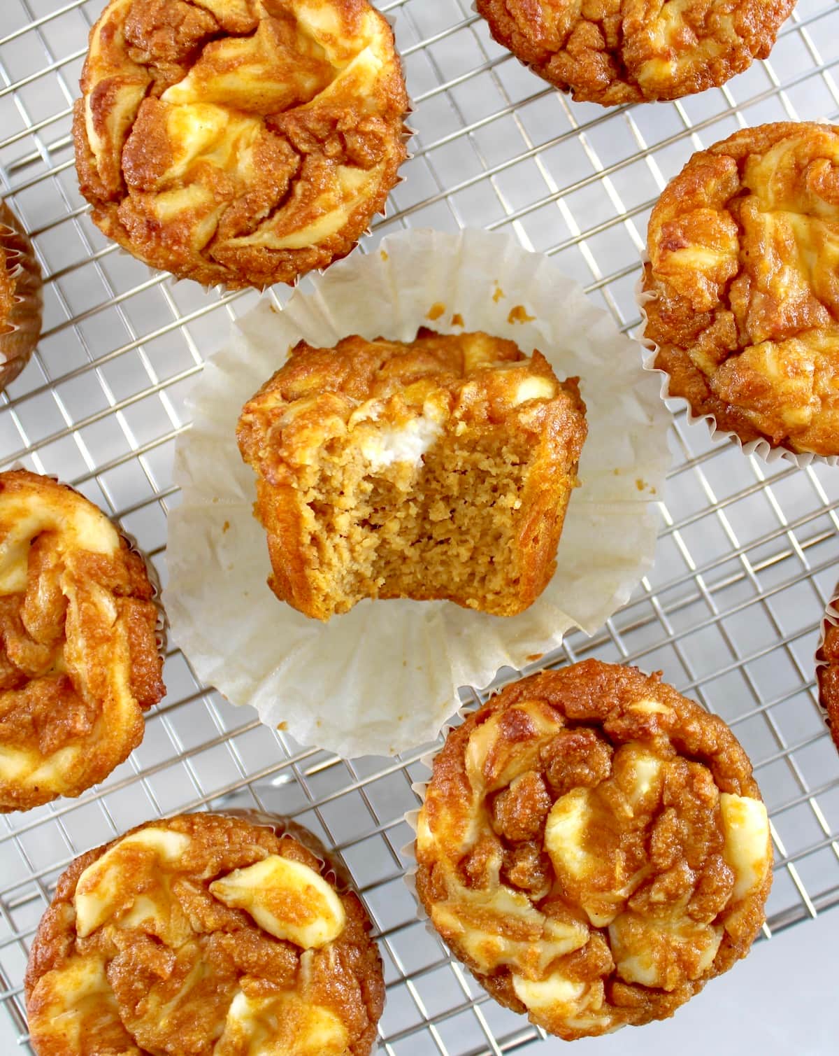 overhead view of Keto Pumpkin Cream Cheese Swirl Muffins on cooling rack with bite missing from center muffin