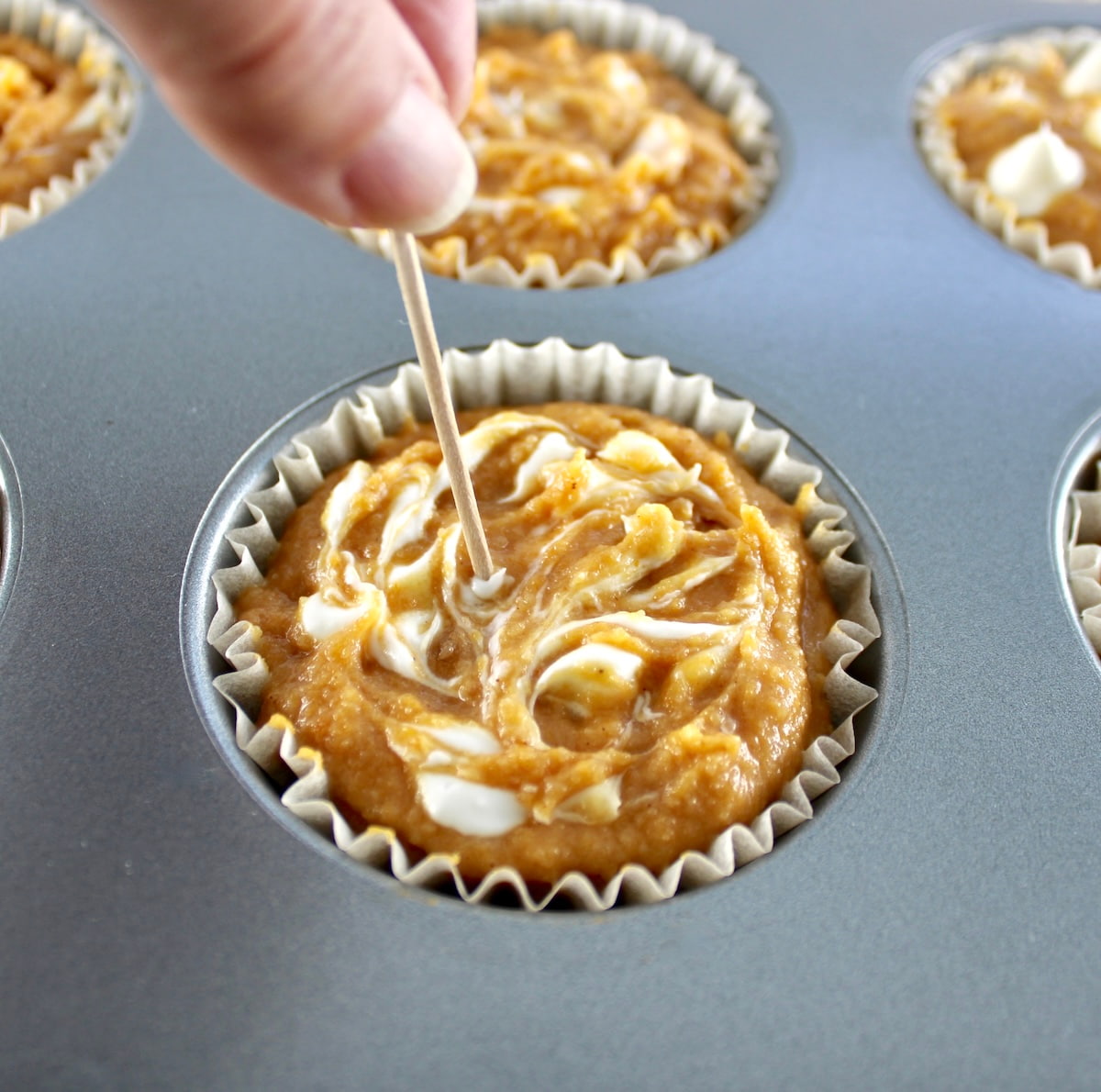 toothpick being swirled in Keto Pumpkin Cream Cheese Swirl Muffin batter