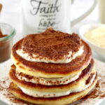 Keto Tiramisu Pancakes stacked on white plate with mug of coffee in back