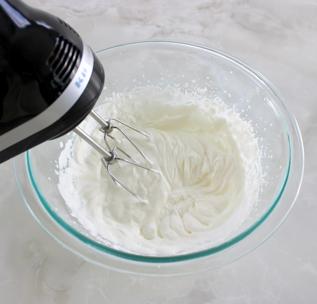 cream being whipped in glass bowl with hand mixer