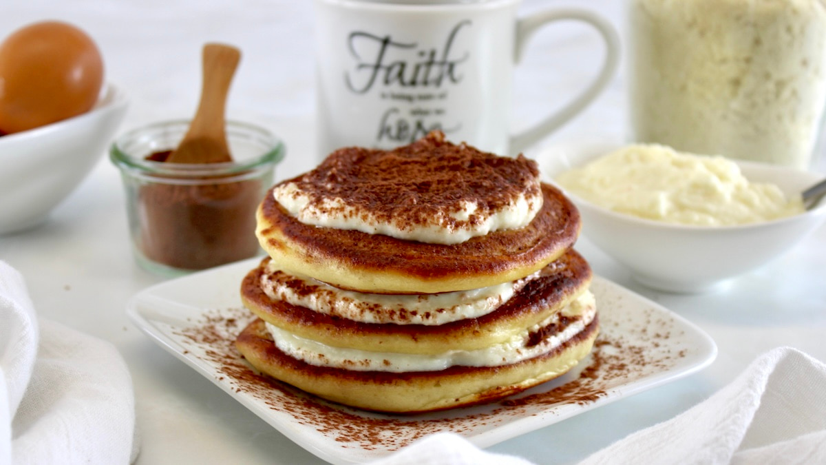 Keto Tiramisu Pancakes stacked on white plate with mug of coffee in back