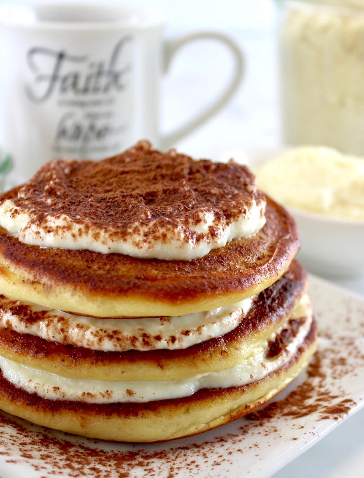 Keto Tiramisu Pancakes stacked on white plate with mug of coffee in back