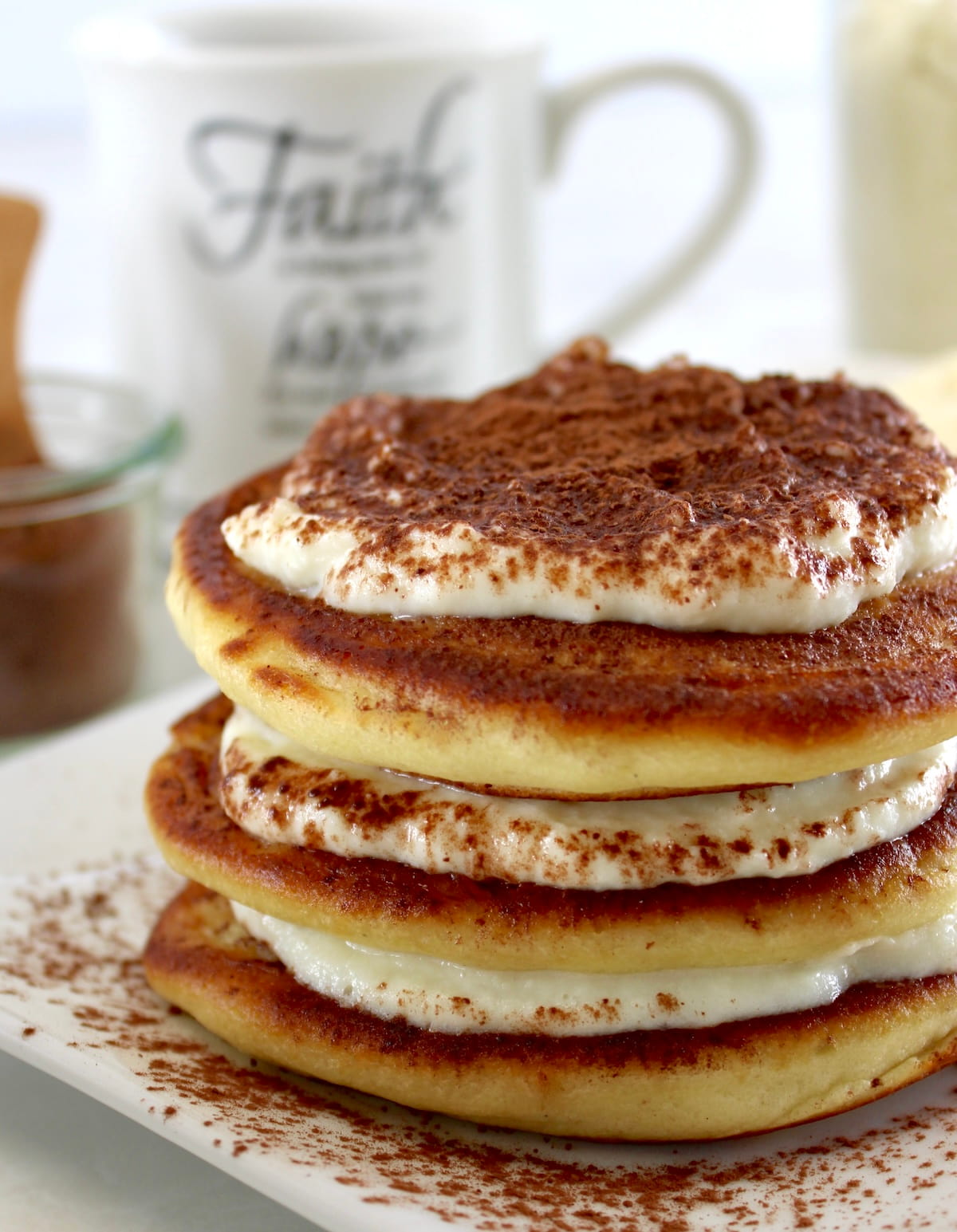 Keto Tiramisu Pancakes stacked on white plate with mug of coffee in back