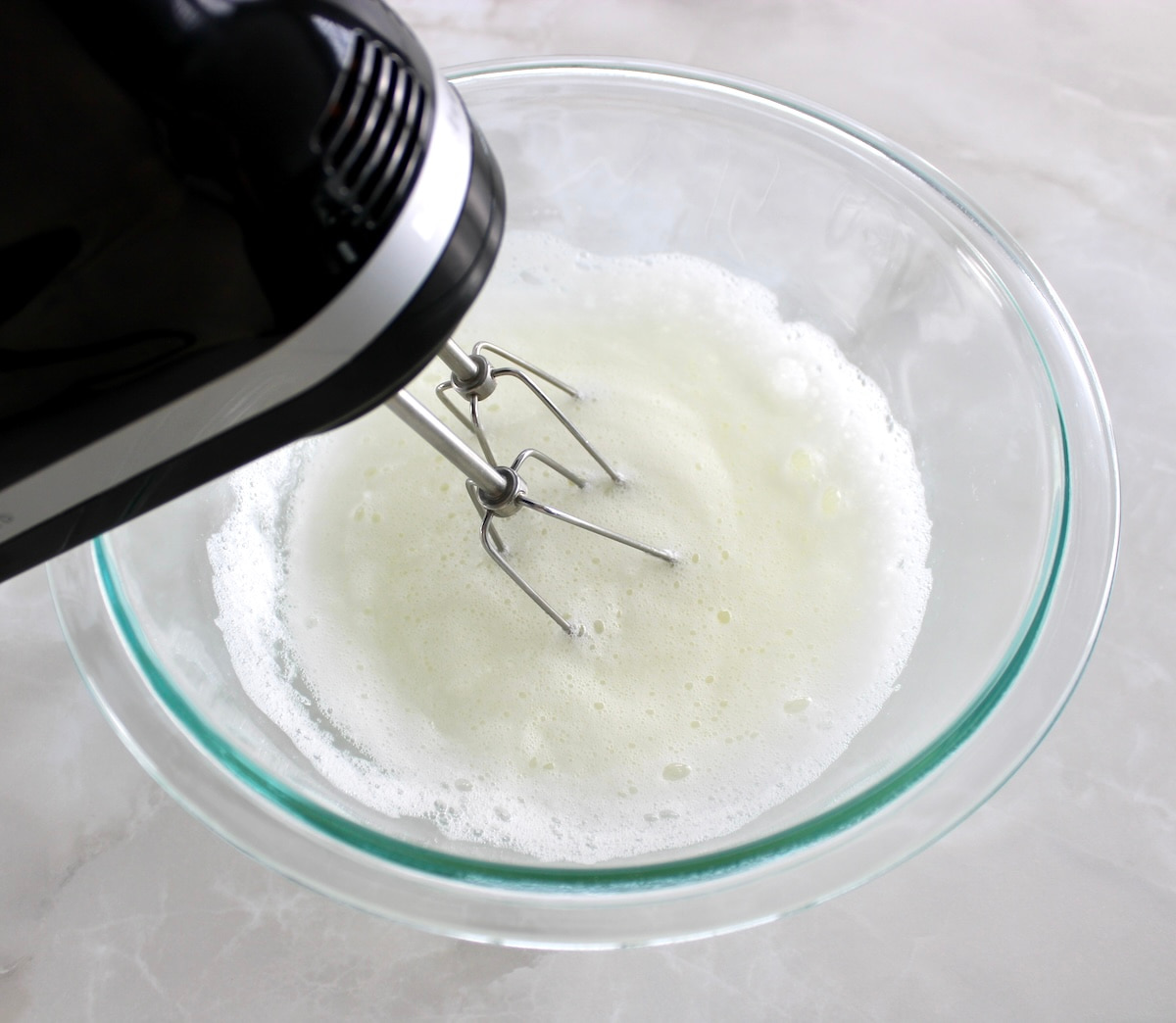 egg whites in glass bowl being whipped with hand mixer