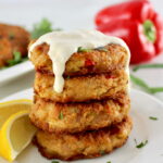 4 Tuna Cakes stacked up on white plate with lemon slices on side and garlic aioli dripping down from the top