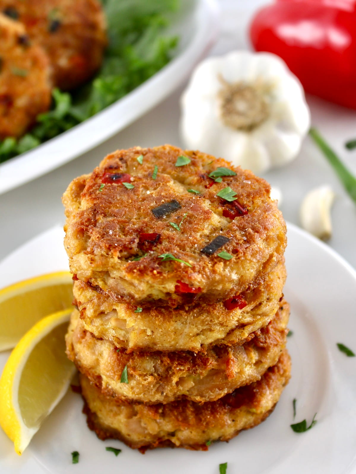 4 Tuna Cakes stacked up on white platter with lemon wedges on side