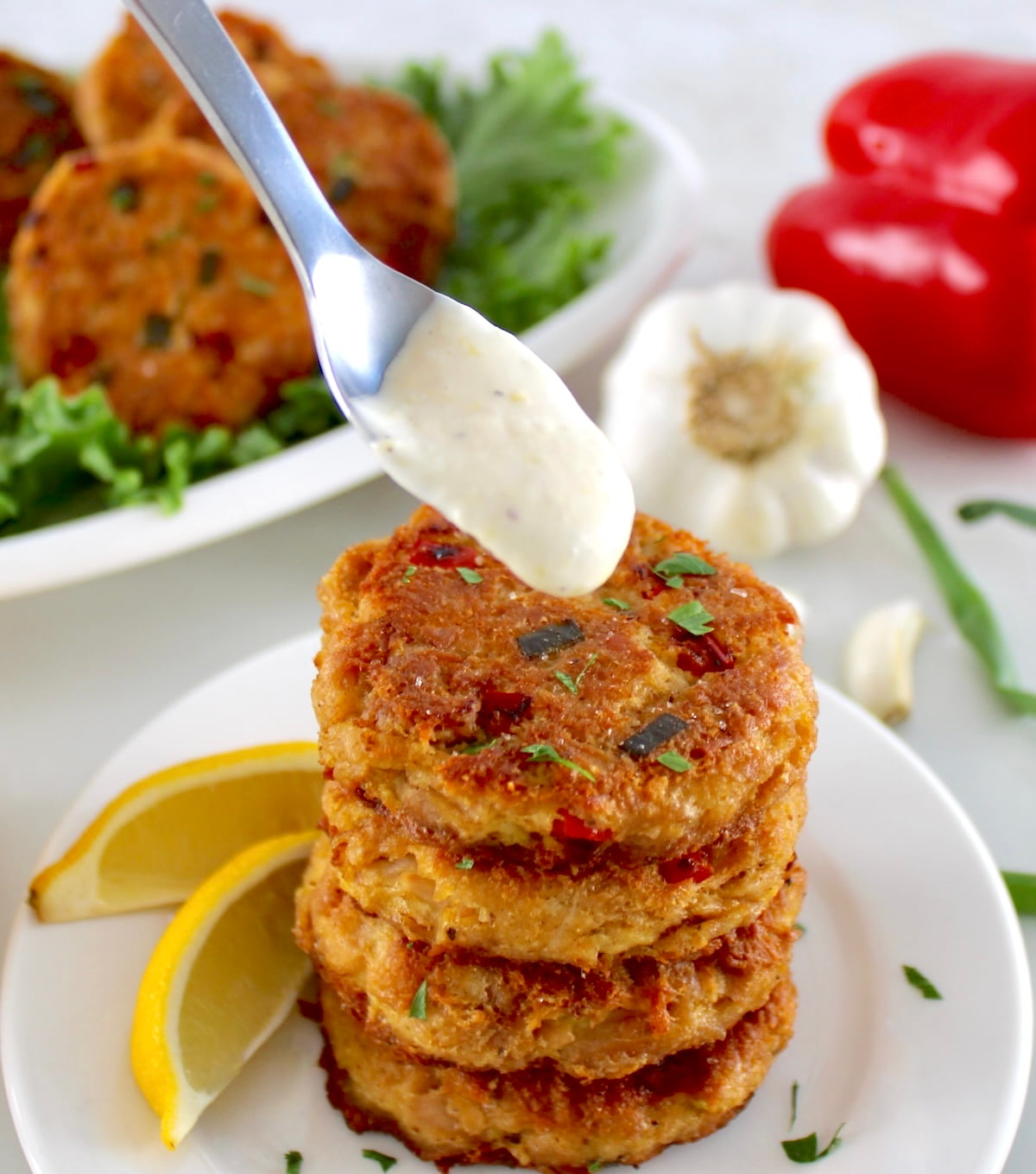 4 Tuna Cakes stacked up on white plate with garlic aioli dripping from spoon over top