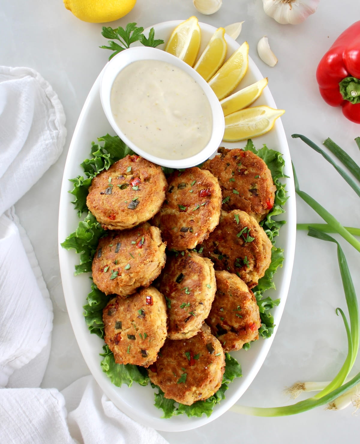 overhead view of Tuna Cakes on white oval platter with garlic aioli and lemon wedges