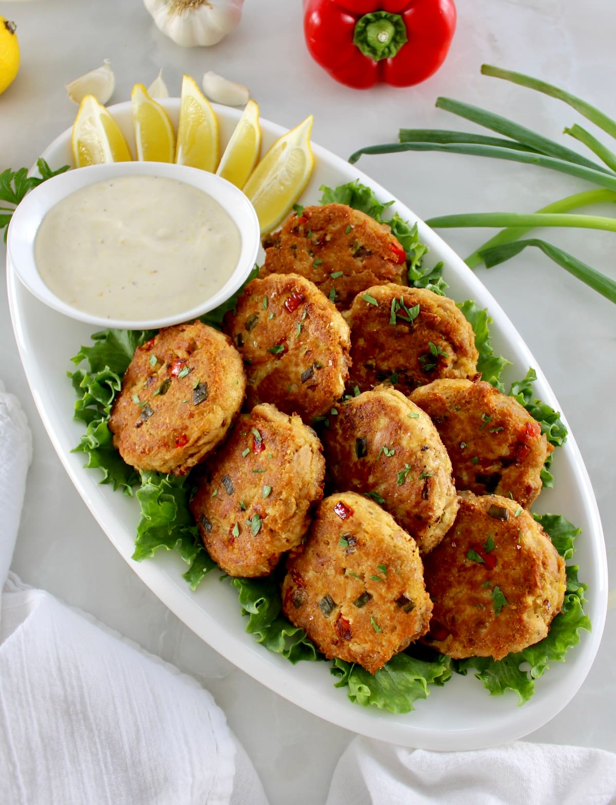 Tuna Cakes on white oval platter with garlic aioli sauce and lemon slices on side