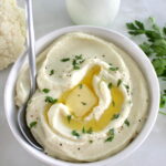 Cottage Cheese Cauliflower Mash in white bowl with melted butter and spoon on side