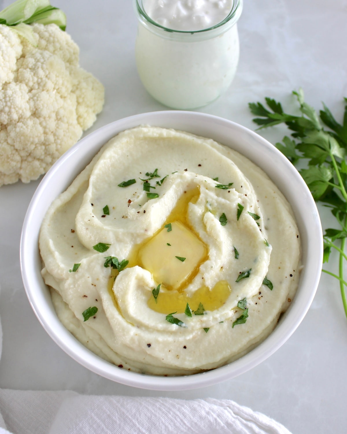 overhead view of Cottage Cheese Cauliflower Mash in white bowl with melted butter and chopped parsley