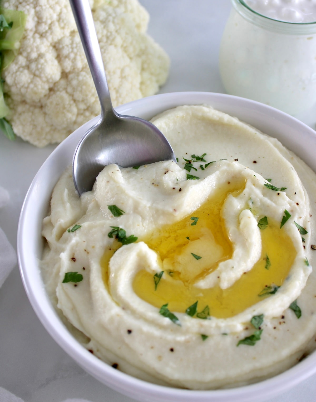 Cottage Cheese Cauliflower Mash in white bowl with melting butter and spoon on side