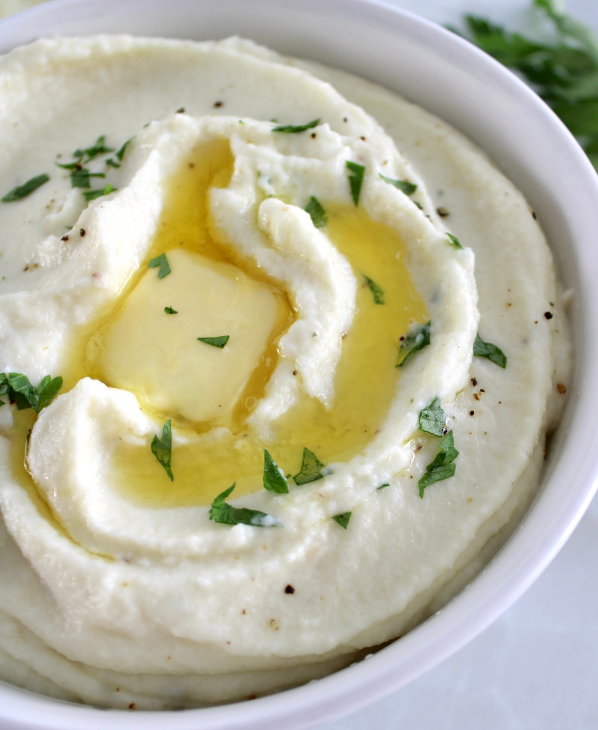 closeup of Cottage Cheese Cauliflower Mash in white bowl with butter and chopped parsley
