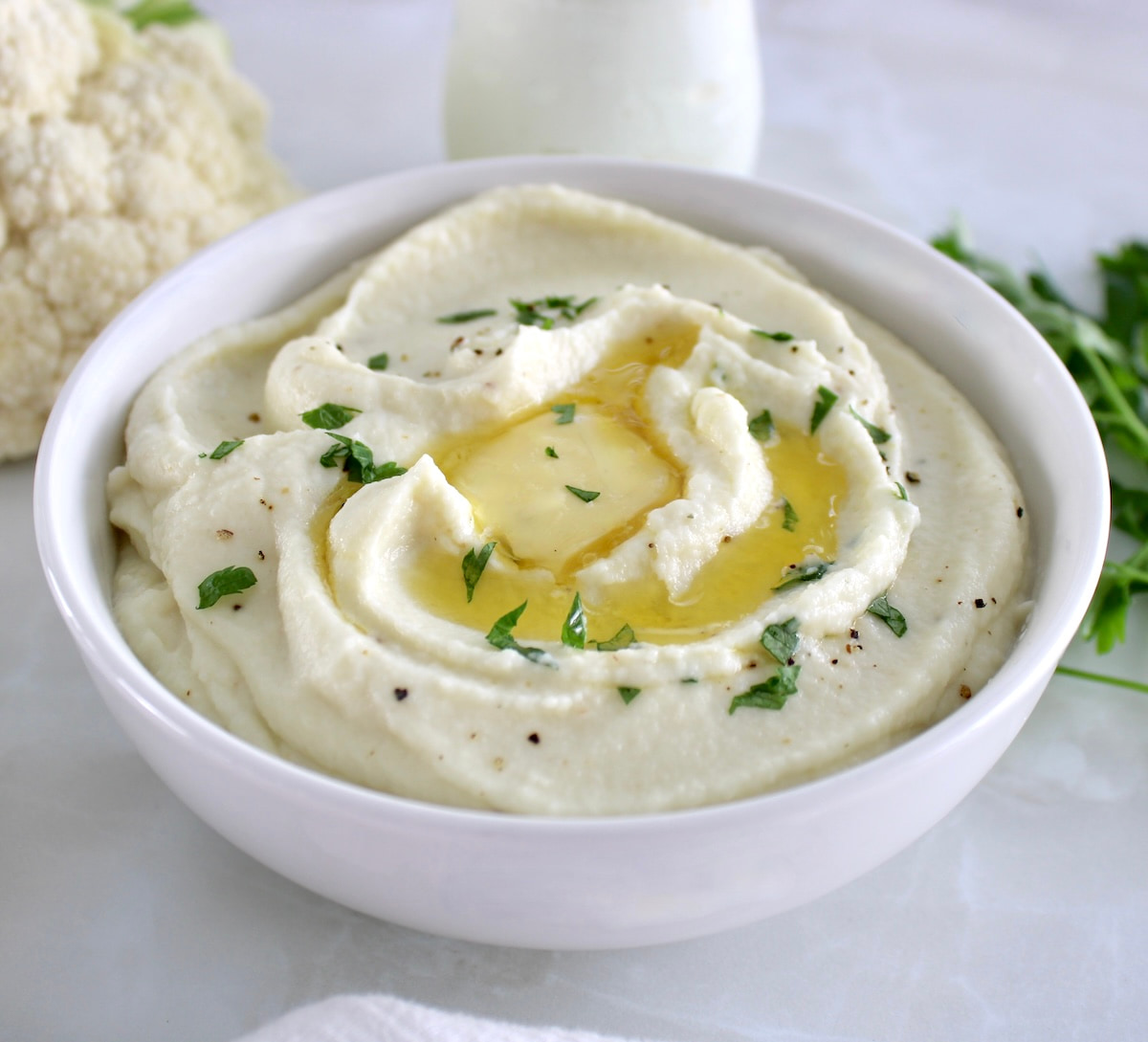 Cottage Cheese Cauliflower Mash in white bowl with melted butter and chopped parsley