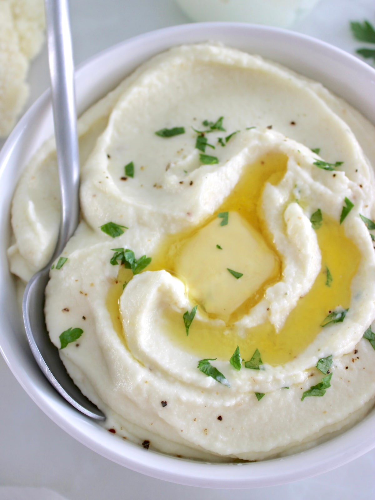 closeup of Cottage Cheese Cauliflower Mash in white bowl with butter melting and spoon on side